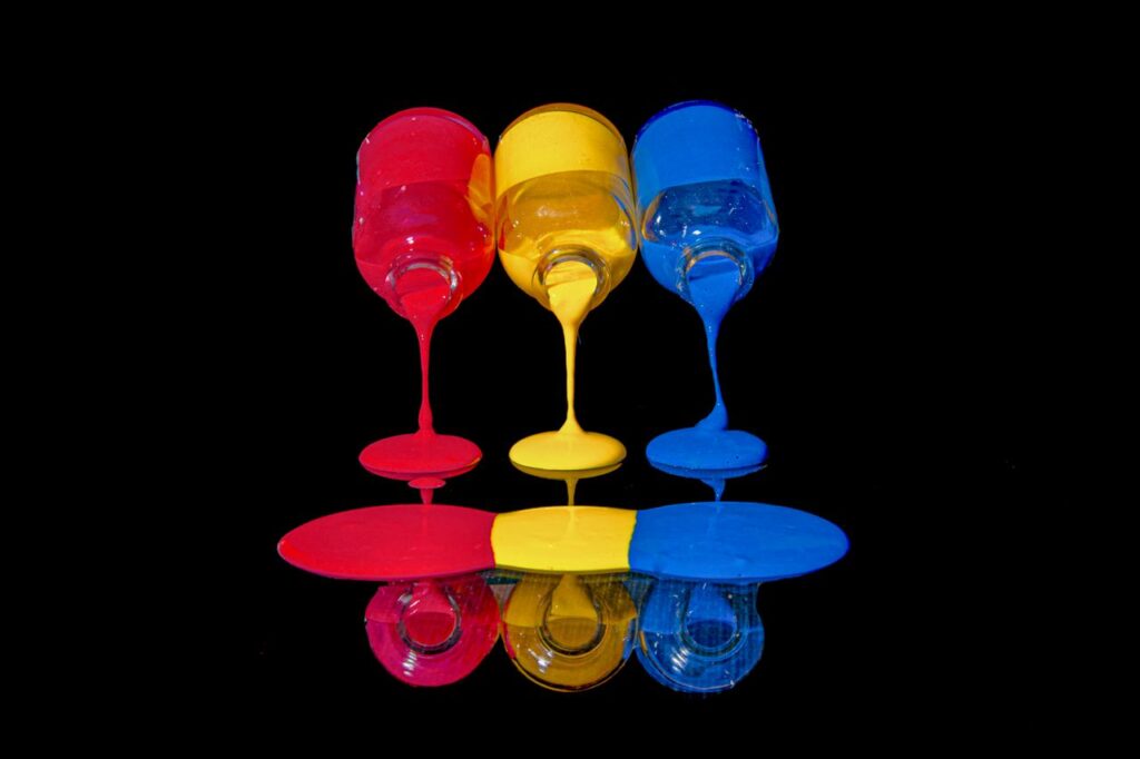 Artistic photograph of red, yellow, and blue paint flowing from glasses, creating a colorful reflection.
