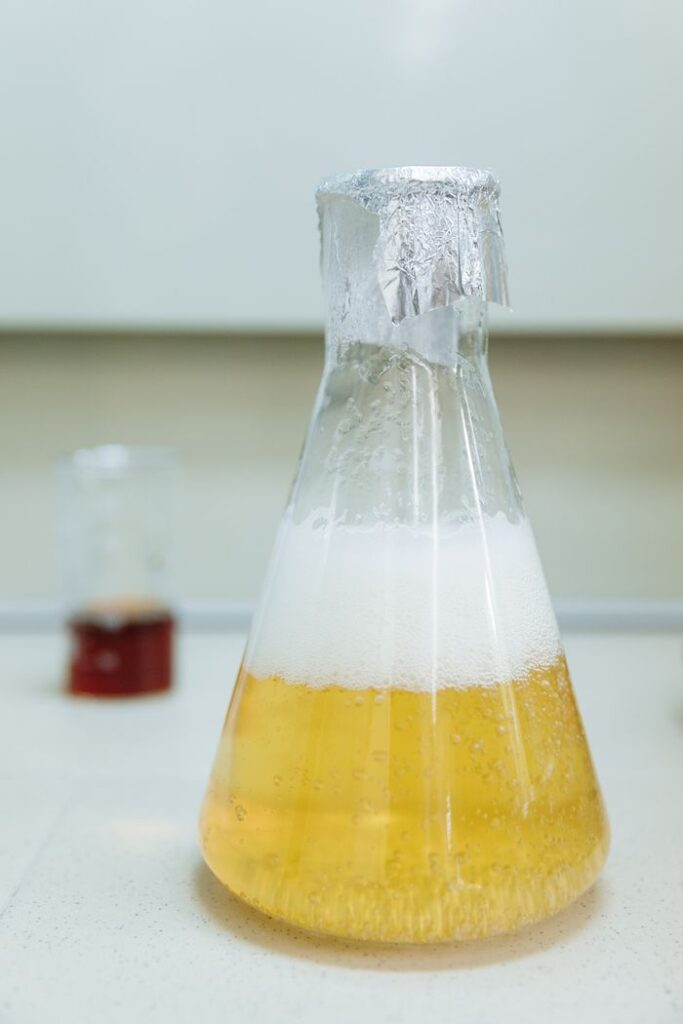 Close-up of a bubbling liquid in an Erlenmeyer flask wrapped with foil, indoors in a lab.